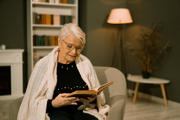 Weise ältere Frau in Brillen, die altes Buch lesen