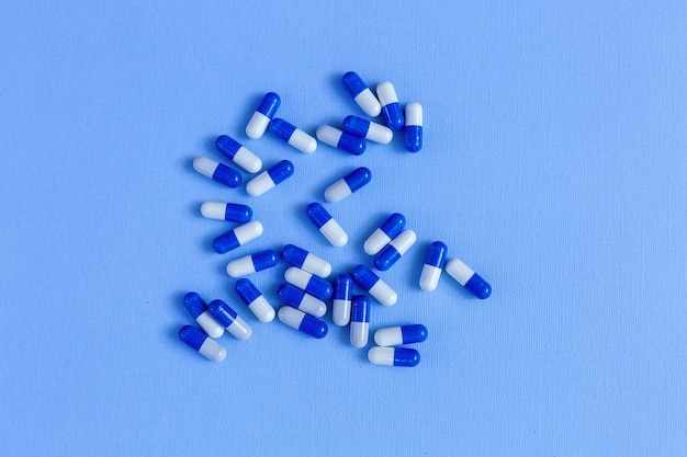 Foto weiß-blaue medizin-kapseln von ovaler form liegen auf einem blauen hintergrund.