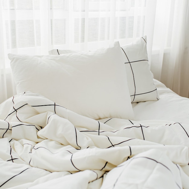 Weiße Bettwäsche mit gestreifter Decke und Kissen. Unordentliches Bett.
