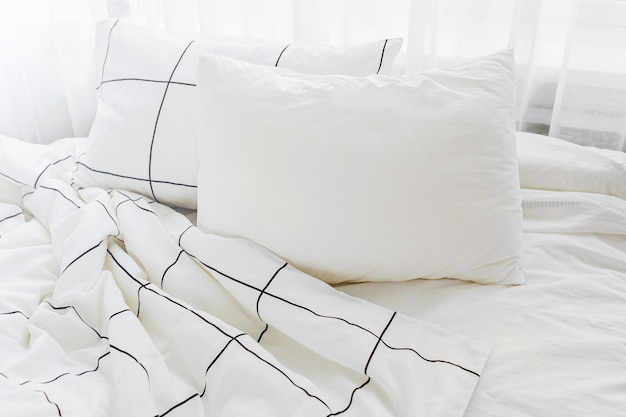 Weiße Bettwäsche mit gestreifter Decke und Kissen. Unordentliches Bett.