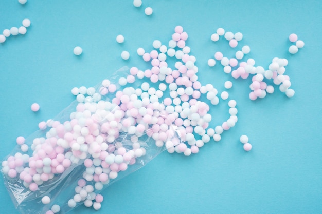 Weiße, blaue und rosa Mini-Pompons-Bälle werden aus einer Plastiktüte auf blauem Hintergrund verschüttet