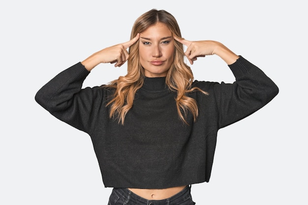 Weiße blonde Frau im Studio konzentriert sich auf eine Aufgabe, die die Zeigefinger auf den Kopf zeigt