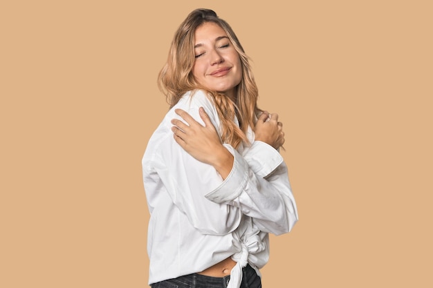 Weiße blonde Frau im Studio umarmt lächelnd sorglos und glücklich