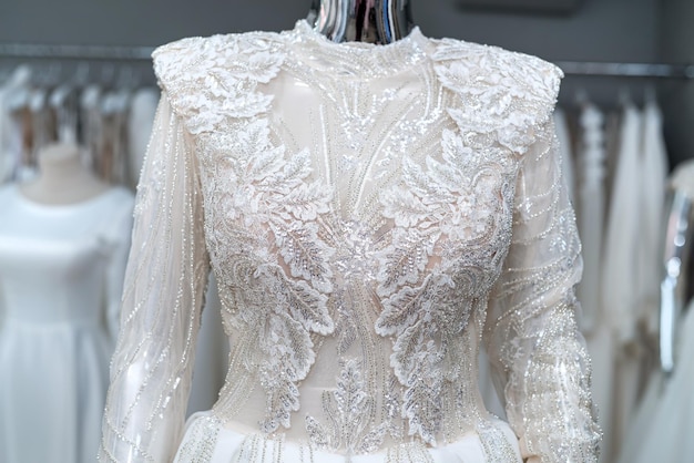 Weiße Brautkleider auf Schaufensterpuppe und hängen an Kleiderbügeln im Ausstellungsraum des Ladens