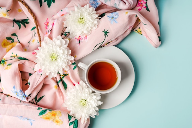 Weiße Chrysanthemenblumen auf einem Frauenhemd und einer Tasse Tee auf einem hellblauen Hintergrund