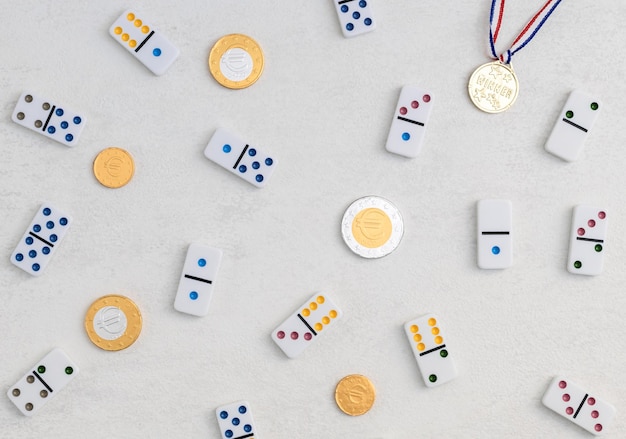 Weiße Dominosteine mit bunten Dotswinner-Medaillen und Schokoladenmünzen auf Draufsicht des weißen Zementhintergrunds Brettspiel