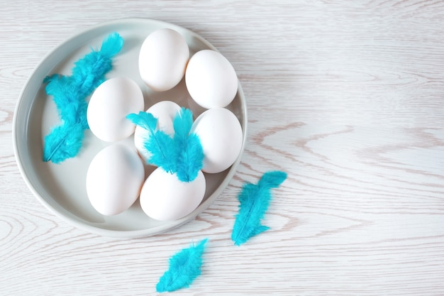 Weiße Eier in einem Teller mit blauen Federn auf weißem Holztisch, Osterkomposition.