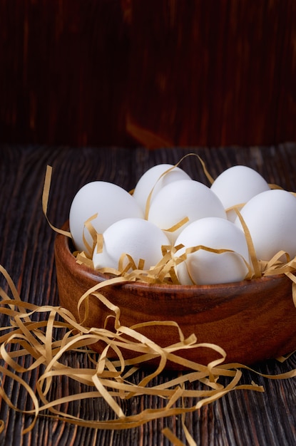 Weiße Eier in einer Holzschale, auf Papierstroh und auf einem Holztisch. Zurückhaltend.