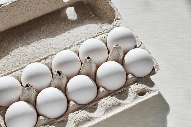 Weiße Eier in Papiereierschachtel Hühnereier Pappeierschachtel auf dem weißen Tisch in Sonnenling mit Schatten Draufsicht