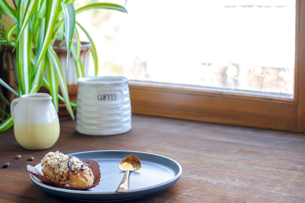 Weiße Espresso-Kaffeetasse, frisch gebackenes Eclair, süßes Dessert auf Teller, Küchentisch, gegen Fenstergeschirr, Geschirr, Milchkännchen, grüne Pflanze, morgens, französisches Frühstück, Kopienraum