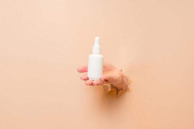 Weiße Flasche mit Serumlotion oder ätherischem Öl Hyaluronsäure und Kollagen in der Hand auf beige Hintergrund Hautpflege-Kosmetik-Konzept Schönheitsflyer