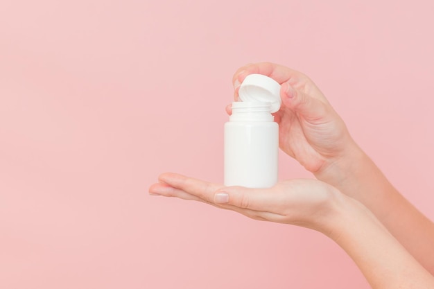 Weiße Flaschen aus Kunststoff in weiblichen Händen auf rosa Hintergrund Verpackungen für Pillen, Kapseln oder Nahrungsergänzungsmittel Kosmetika