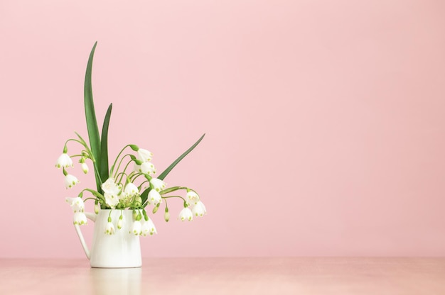 Weiße Frühlingsblumen im Krug auf rosa Hintergrund