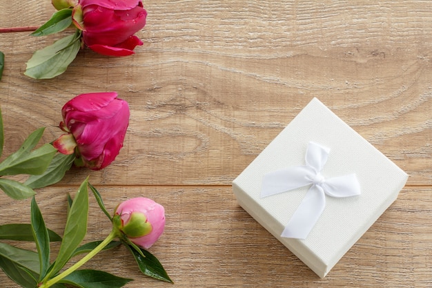 Weiße Geschenkbox auf Holzbrettern, verziert mit Pfingstrosenblüten.