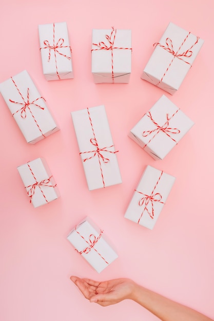 Weiße Geschenkboxen mit rotem Band auf einem rosa Hintergrund, Frauenhände halten eine weiße Box