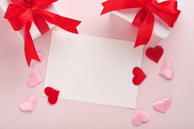 Weiße Geschenkboxen mit rotem Band und kleinen roten dekorativen Herzen auf rosa Hintergrund. Draufsicht mit Kopienraum. Valentinstag oder Hochzeit romantisches Konzept. Festliche Komposition. Attrappe, Lehrmodell, Simulation.