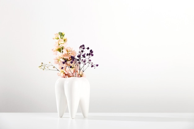 Weiße große Zahnvase mit Blumen auf weißem Hintergrund und kieferorthopädischer Zahnarztästhetik