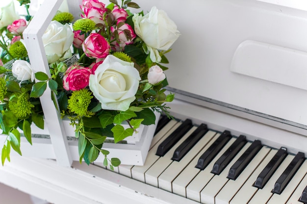 Weiße Holzkiste mit weißen und rosa Rosenstrauß und Chrysanthemen auf weißem Klavier. Dekoration von zu Hause. Blumenkästen. Hochzeitsdekoration