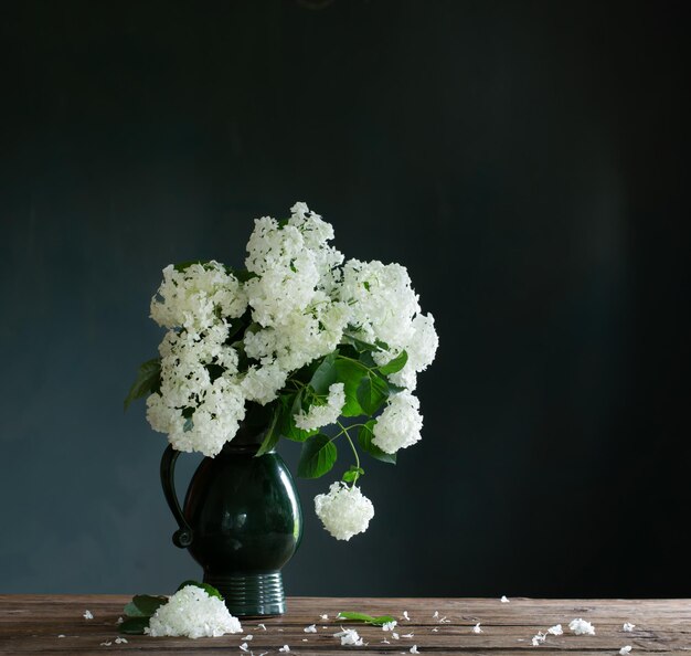 Weiße Hortensie im Vintage-Krug auf Holztisch auf dunkler Hintergrundwand
