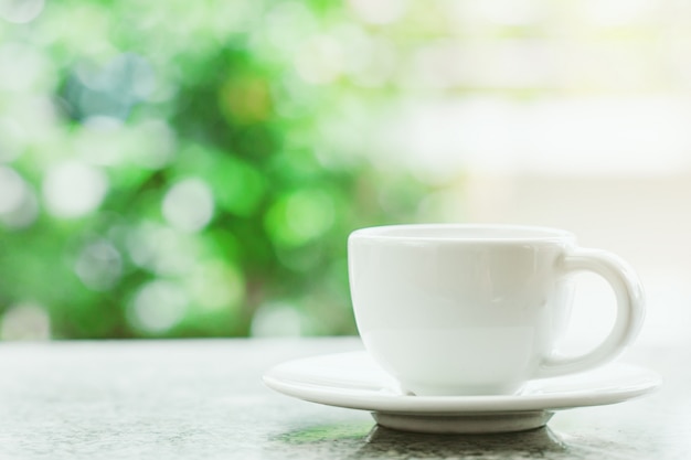 Weiße Kaffeetasse gegen unscharfen natürlichen grünen Hintergrund