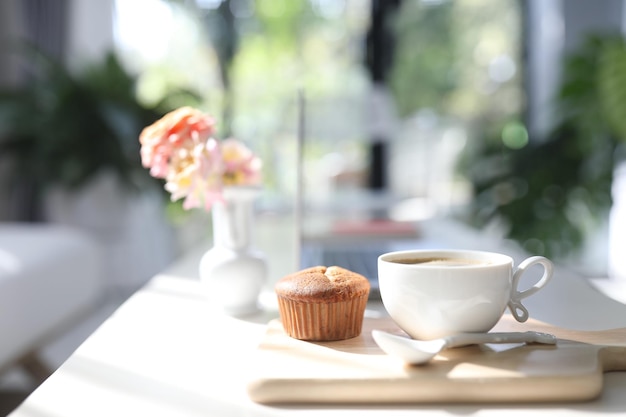 Weiße Kaffeetasse und Cupcake und Rosenvase auf Holztablett