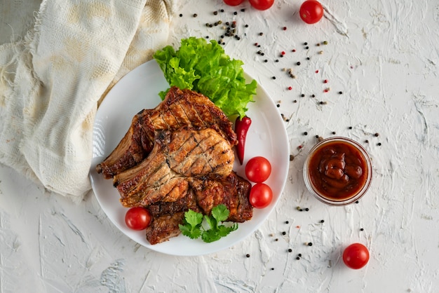 Weiße Keramikplatte mit gegrilltem Schweinefleisch, Salatblättern, Tomate und glühendem Pfeffer und Soße in den Schüsseln