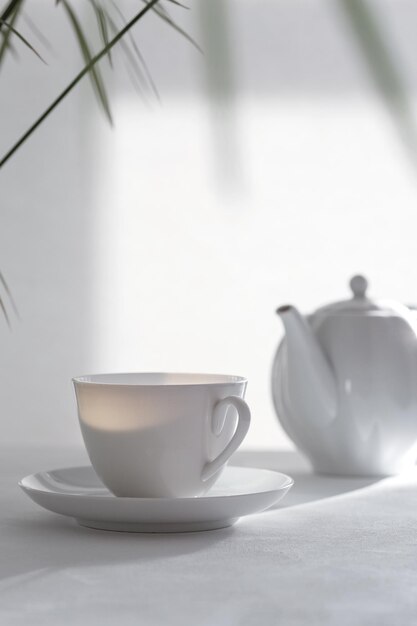 Weiße Keramiktasse und Teekanne auf dem Tisch Natürliche Beleuchtung, helle Sonne aus dem Fenster