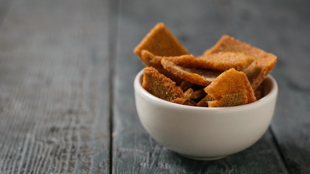 Weiße keramische Schüssel mit Stücken getrocknetem Brot auf einem schwarzen Holztisch.