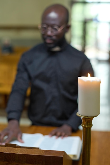 Weiße Kerze, die gegen jungen afroamerikanischen Pastor brennt, der Bibel liest