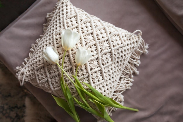 Weiße Kissen mit Makramee-Bett in einem minimalistischen Schlafzimmer im skandinavischen Stil Weiße Tulpe auf Makramee-Kissen