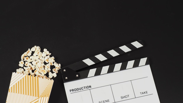 Weiße Klappe oder Filmtafel und eine Schachtel Popcorn auf schwarzem Hintergrund x9