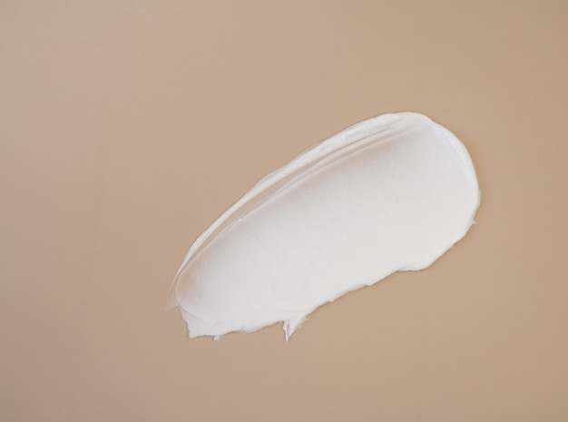 Weiße kosmetische Cremeabstriche auf einem dunkelbeigen Hintergrund Gesichtslotion Abstrichserum die Textur