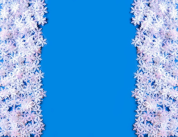 Foto weiße künstliche schneeflocken auf weichem blauem hintergrund. symmetrischer hintergrund des winters. dekorative vorlage für karten, banner, poster.