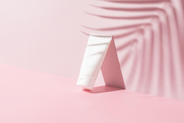 Weiße Kunststoffröhre für Creme spf oder Lotion Hautpflege oder Sonnenschutzkosmetik auf rosa Hintergrund mit Palmblättern Schatten Schönheitskonzept für die Gesichtspflege
