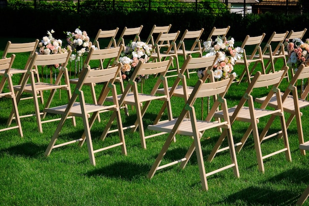 Weiße leere Holzstühle in einer Reihe und Blumensträuße auf grünem Gras.