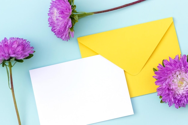 Weiße leere Karte gelber Umschlag und violette Blume auf blauem Hintergrund Minimaler Stil Draufsicht Flaches Lay-Mockup