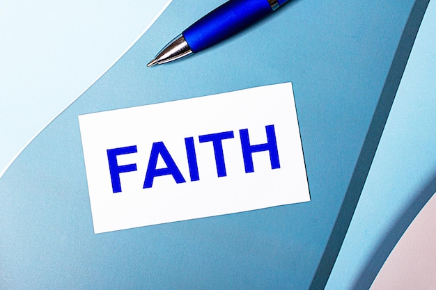 Weiße leere Karte mit FAITH-Text und blauem Stift auf blauem cyan-blauem und rosafarbenem Hintergrund