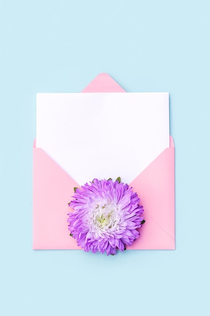 Weiße leere Karte rosa Umschlag und Blumen auf blauem Hintergrund Minimaler Stil Draufsicht Flaches Lay-Mockup