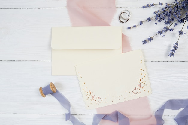 Weiße leere Karte, Umschlag und Band mit zwei Eheringen auf rosa Gewebe