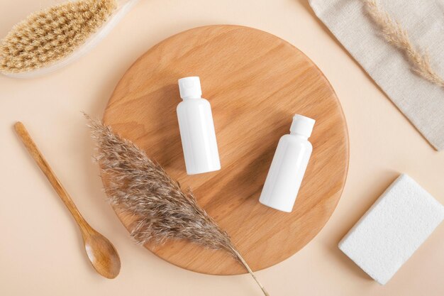 Weiße leere Kosmetikflaschen getrocknete Kräuter auf Holzplatte Natürliche Hautpflege SPA Beauty Produktdesign Mineralische Bio-Kosmetik MockUp Beige Hintergrund Gesichts- und Körperbehandlung Flache Ansicht von oben