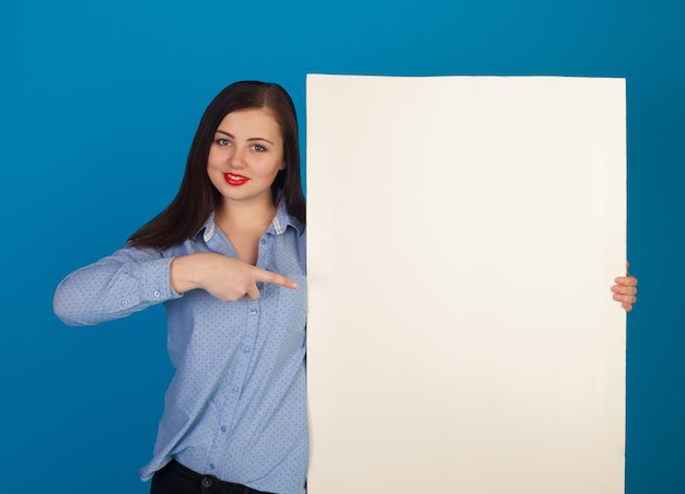 Weiße Leinwand wird von einer süßen Frau mit roten Lippen vor blauem Hintergrund gehalten