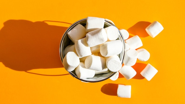 Weiße Marshmallows in einem weißen Metalleimer auf einem gelben Hintergrundkopierraum, eine Zutat für die Herstellung eines Weihnachtsgetränks und die Dekoration von Kuchen. Ungesundes Junk-Essen.