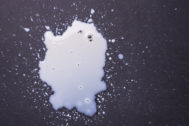 Weiße Milch verschüttete und spritzt auf der dunklen Bodenoberfläche. Draufsicht