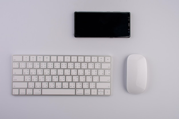 Weiße minimalistische und stilvolle Tastaturmaus und Moblie auf weißem Tisch