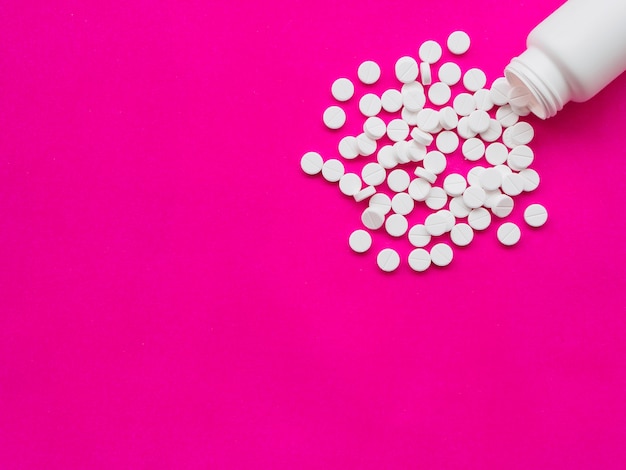 Weiße Pillen, die aus einer weißen Tablettenfläschchen heraus verschüttet werden