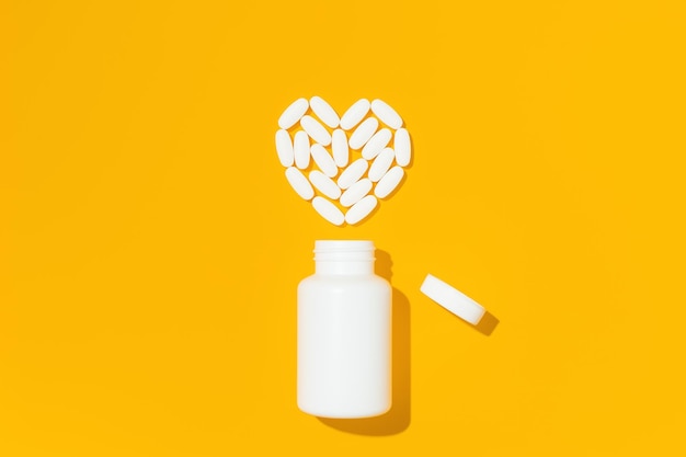 Weiße Pillen in Herzform mit Flasche auf gelbem Hintergrund Mockup für Werbung oder andere Ideen Medizin- und Gesundheitskonzept
