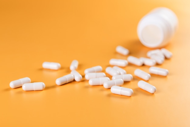 Weiße Pillen, Tabletten oder Kapseln der pharmazeutischen Medizin auf gelbem Hintergrund.