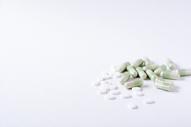 Weiße Pillen und grüne Kapseln auf weißer Oberfläche