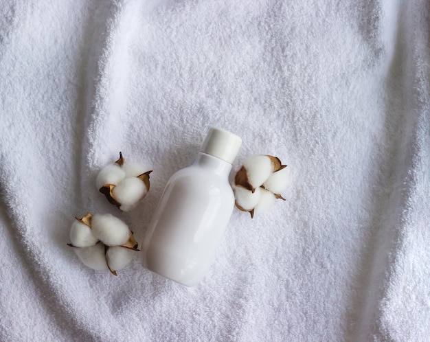 Weiße Plastikflasche für Kosmetika mit Baumwollblumen auf dem weißen Handtuch