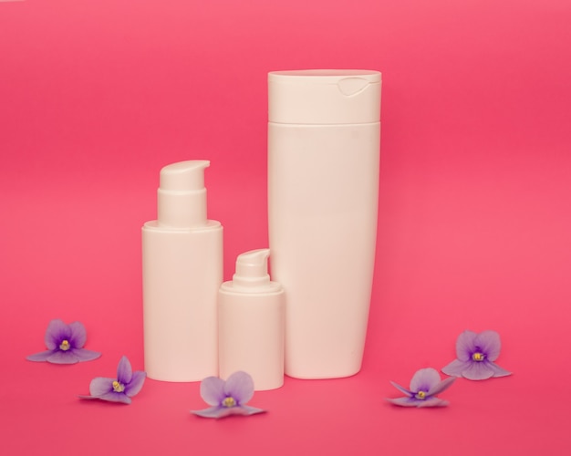 Weiße Plastikflaschen auf einem rosa Hintergrund, ein Satz Kosmetikbehälter mit einem Spender. Kopierplatz, leerer Platz für Text. Toilettenartikel, Pumpenlotion. Feuchtigkeitscreme für Körper und Gesicht.